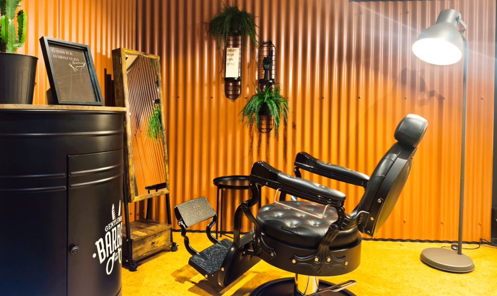 Chaise de barbier en cuir noir au centre de l'image. Style industriel. Fond en panneaux ondulés couleur terracotta